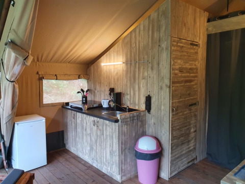 Interior view of a safari tent with wooden kitchen, fridge, and bin at Camping het Horstmannsbos in the Netherlands.