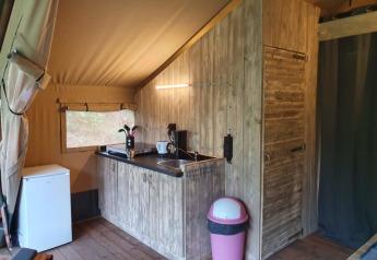 Vista interior de una tienda safari con cocina de madera, nevera y cubo en Camping het Horstmannsbos, Países Bajos.