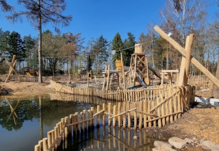 Parco giochi in legno con scivolo e acqua al Camping het Horstmannsbos, Paesi Bassi, in una giornata di sole.