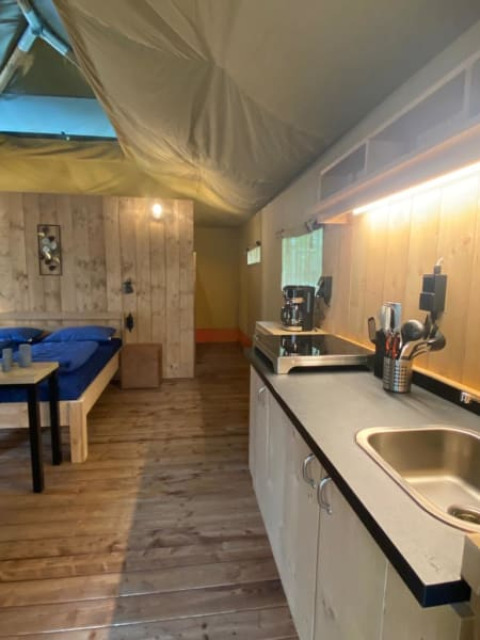 Interno di una tenda safari di lusso con letto, cucina e pavimento in legno al Camping het Horstmannsbos, Paesi Bassi.