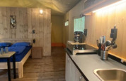 Interior of a luxe safari tent with bed, kitchenette and wooden floor at Camping het Horstmannsbos, Netherlands.