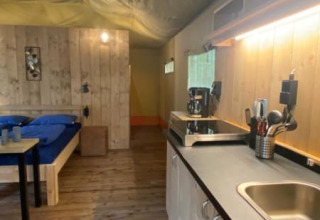 Interior de una tienda safari de lujo con cama, cocina y suelo de madera en Camping het Horstmannsbos, Países Bajos.