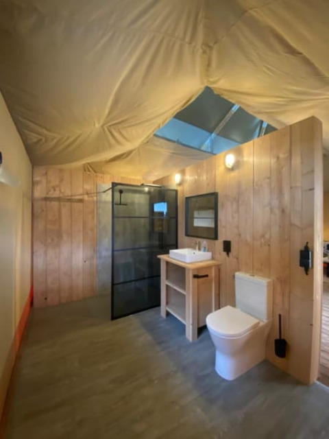 Modern bathroom with wood walls, shower, and tent ceiling inside Luxe Safari tent in the Netherlands