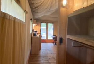 Vista interior de una tienda safari de lujo con suelo de madera y paredes de lona en Camping het Horstmannsbos.