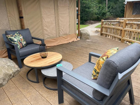 Gemütliche Terrasse mit grauen Sesseln, Holztisch und Kissen vor einem Luxus-Safari-Zelt auf Camping het Horstmannsbos.