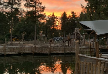 Sunset over a lake with trees and wooden decks at Safari tent Zeelt in Camping het Horstmannsbos, Netherlands.