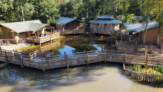 Safari tents by a pond with wooden walkways, surrounded by forest, perfect for a unique glamping stay.