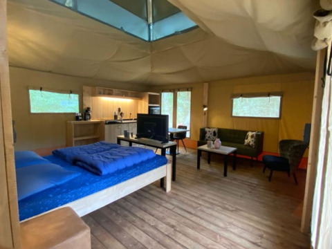 Interno di una tenda safari di lusso con cucina, letto e area relax al Camping het Horstmannsbos, Olanda.