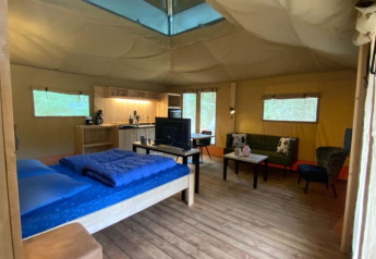 Interior of a luxe safari tent with kitchen, bed, and lounge area at Camping het Horstmannsbos, Netherlands.