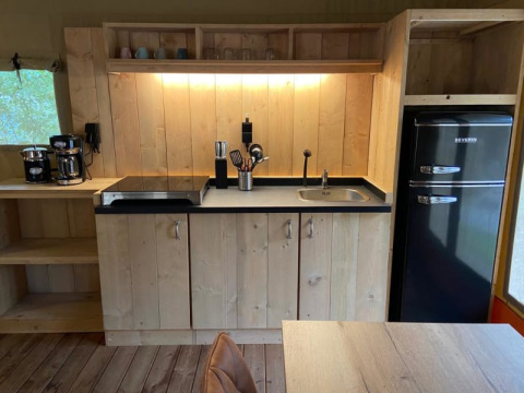 Kitchen area in a luxe safari tent with modern appliances and wood paneling at Camping het Horstmannsbos, Netherlands.