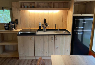 Cocina en una tienda safari de lujo con electrodomésticos modernos y paneles de madera en Camping het Horstmannsbos.