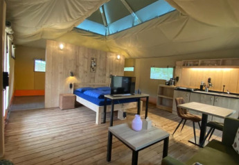 Interno di una tenda safari di lusso con pavimento in legno, mobili moderni e un piccolo angolo cottura.