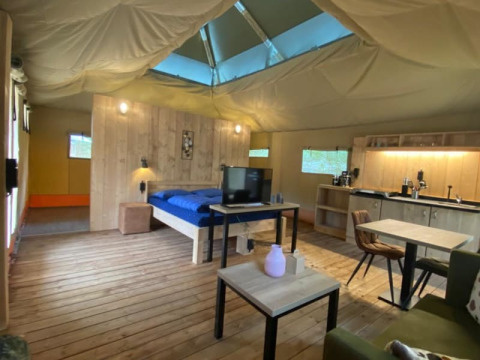 Interno di una tenda safari di lusso con pavimento in legno, mobili moderni e un piccolo angolo cottura.