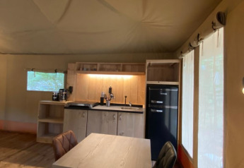Interior de una tienda safari de lujo con cocina, mesa de comedor y ventanas en Camping het Horstmannsbos, Países Bajos.