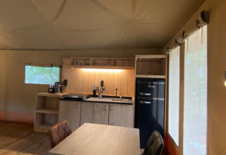 Interior of a luxe safari tent with kitchenette, dining table, and windows at Camping het Horstmannsbos, Netherlands.