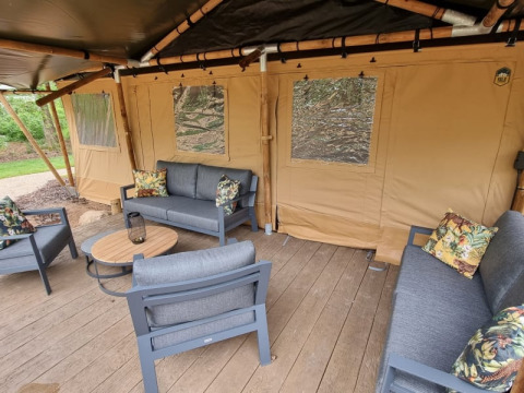 Buitenlounge met comfortabele banken en houten terras voor een luxe safaritent bij Horstmannsbos, Nederland.
