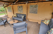 Area salotto all'aperto con divani moderni su terrazza in legno davanti a tenda safari in campeggio olandese.
