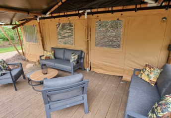 Zona lounge exterior con sofás modernos y tarima de madera junto a tienda safari de lujo en los Países Bajos.