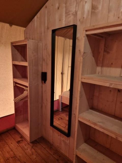 Interior of a safari tent with wooden floor, shelves, and a mirror at Camping het Horstmannsbos, Netherlands.