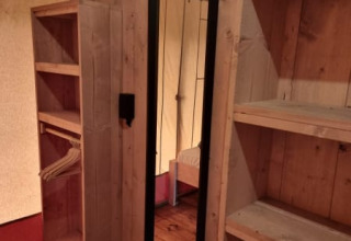 Interior of a safari tent with wooden floor, shelves, and a mirror at Camping het Horstmannsbos, Netherlands.