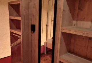 Interior de una tienda safari con suelo de madera, estantes y espejo en Camping het Horstmannsbos, Países Bajos.