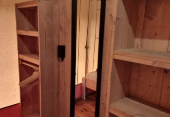 Interior de una tienda safari con suelo de madera, estantes y espejo en Camping het Horstmannsbos, Países Bajos.