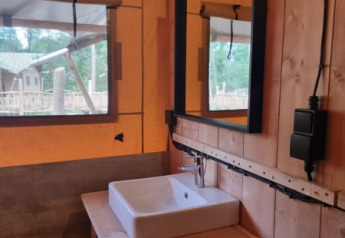 Lavabo y espejo dentro de una tienda safari con paredes de madera en Camping het Horstmannsbos, Países Bajos.