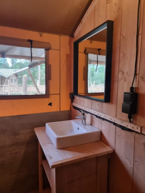 Wastafel en spiegel in een safaritent met houten wanden op Camping het Horstmannsbos in Nederland.