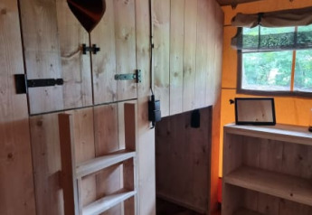 Interior de tienda safari con paredes de madera, estantería y escalera en Camping het Horstmannsbos, Países Bajos.