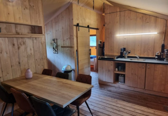 Vista interior de la tienda Safari en Camping het Horstmannsbos, con zona de comedor, cocina y suelos de madera.