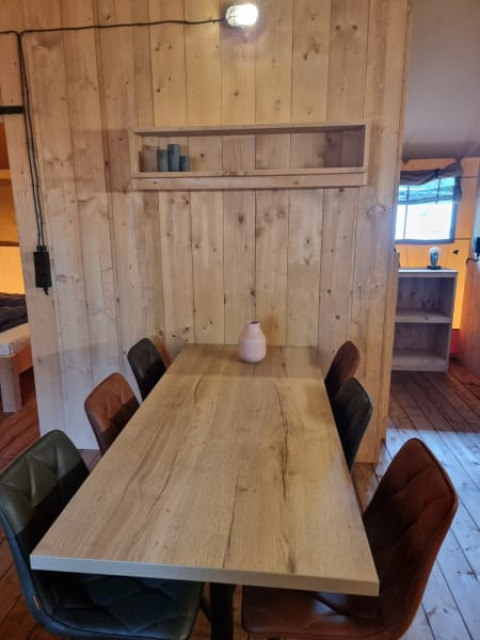 Wooden table with six padded chairs inside a safari tent at Camping het Horstmannsbos in the Netherlands.