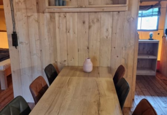 Wooden table with six padded chairs inside a safari tent at Camping het Horstmannsbos in the Netherlands.