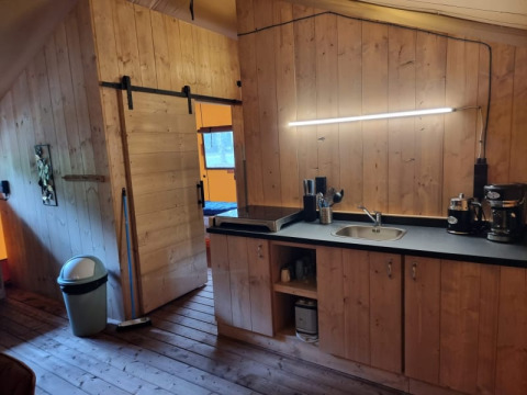 Vista interior de tienda safari en Camping het Horstmannsbos, Países Bajos, con paredes de madera y cocina.