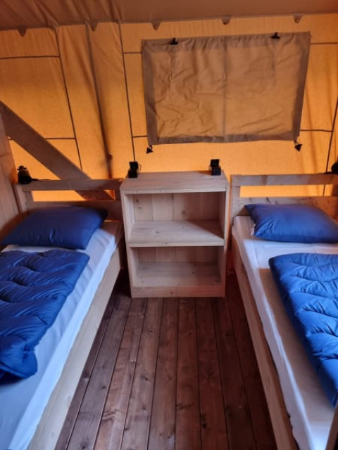 Vista interior de una tienda safari con dos camas individuales, ropa de cama azul y suelo de madera en Holanda.