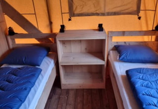 Vista interior de una tienda safari con dos camas individuales, ropa de cama azul y suelo de madera en Holanda.