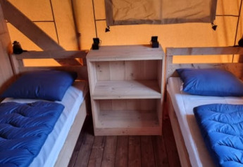Vista interior de una tienda safari con dos camas individuales, ropa de cama azul y suelo de madera en Holanda.