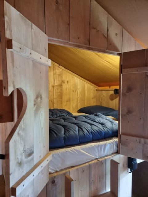 Cozy bed with blue comforter in a wood-paneled safari tent at Camping het Horstmannsbos, Netherlands.