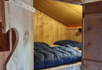 Cama acogedora con edredón azul en una tienda tipo safari de madera en Camping het Horstmannsbos, Países Bajos.