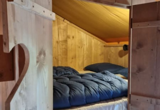 Cama acogedora con edredón azul en una tienda tipo safari de madera en Camping het Horstmannsbos, Países Bajos.