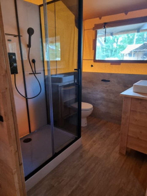 Baño en tienda safari con ducha, inodoro y ventana en Camping het Horstmannsbos en los Países Bajos.