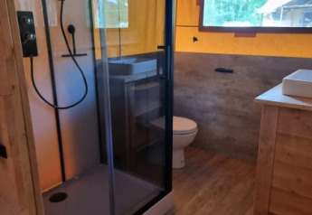 Baño en tienda safari con ducha, inodoro y ventana en Camping het Horstmannsbos en los Países Bajos.