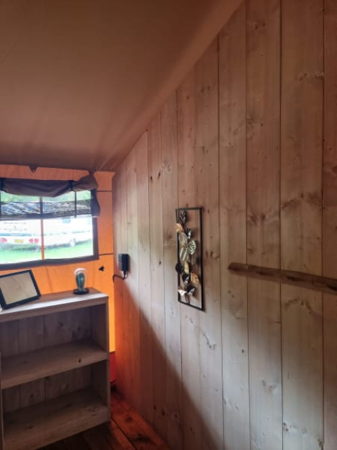 Interior de una tienda safari con paredes de madera y estantería en Camping het Horstmannsbos, Países Bajos.