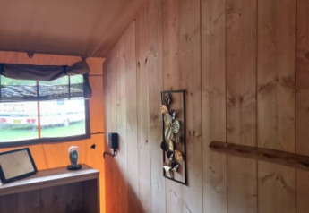 Interior de una tienda safari con paredes de madera y estantería en Camping het Horstmannsbos, Países Bajos.