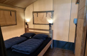 Interior de una tienda safari con cama doble, lámparas y suelo de madera en Camping het Horstmannsbos, Países Bajos.
