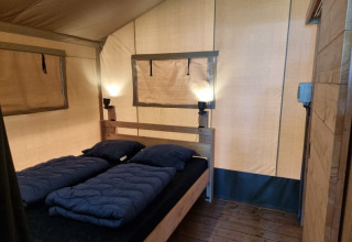 Interno di una tenda safari con letto matrimoniale, lampade e pavimento in legno al Camping het Horstmannsbos nei Paesi Bassi.