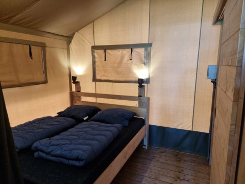 Interno di una tenda safari con letto matrimoniale, lampade e pavimento in legno al Camping het Horstmannsbos nei Paesi Bassi.