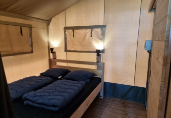 Interior de una tienda safari con cama doble, lámparas y suelo de madera en Camping het Horstmannsbos, Países Bajos.