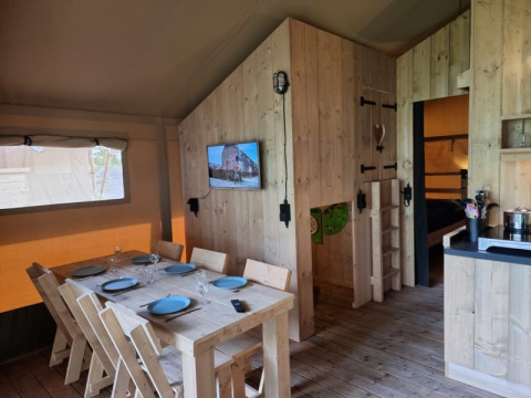 Interno di una tenda safari con area pranzo, TV e cucina al Camping het Horstmannsbos nei Paesi Bassi.