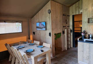 Interior de una tienda safari con mesa de comedor, TV y cocina en Camping het Horstmannsbos, Países Bajos.