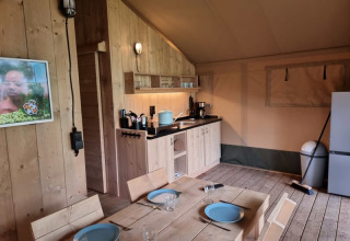 Interior de una tienda safari con muebles de madera, cocina americana y mesa en Camping het Horstmannsbos.
